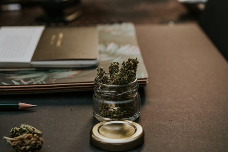 A close-up image of cannabis buds in a glass container on a desk, emphasizing a natural and relaxed setting