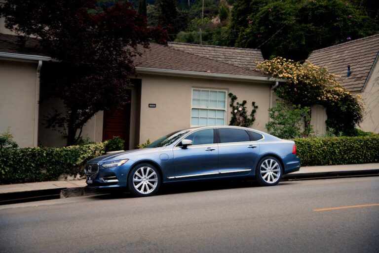 A sleek blue luxury car parked in front of a suburban house with greenery