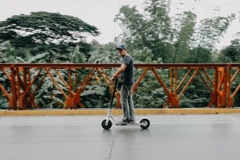 Adult man rides an electric scooter across a bridge surrounded by greenery